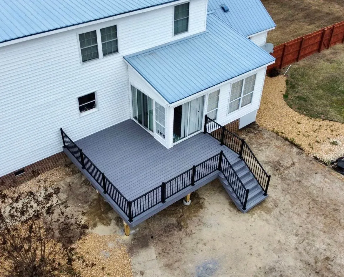 Gray composite deck with black railing connected to a windowed sunroom