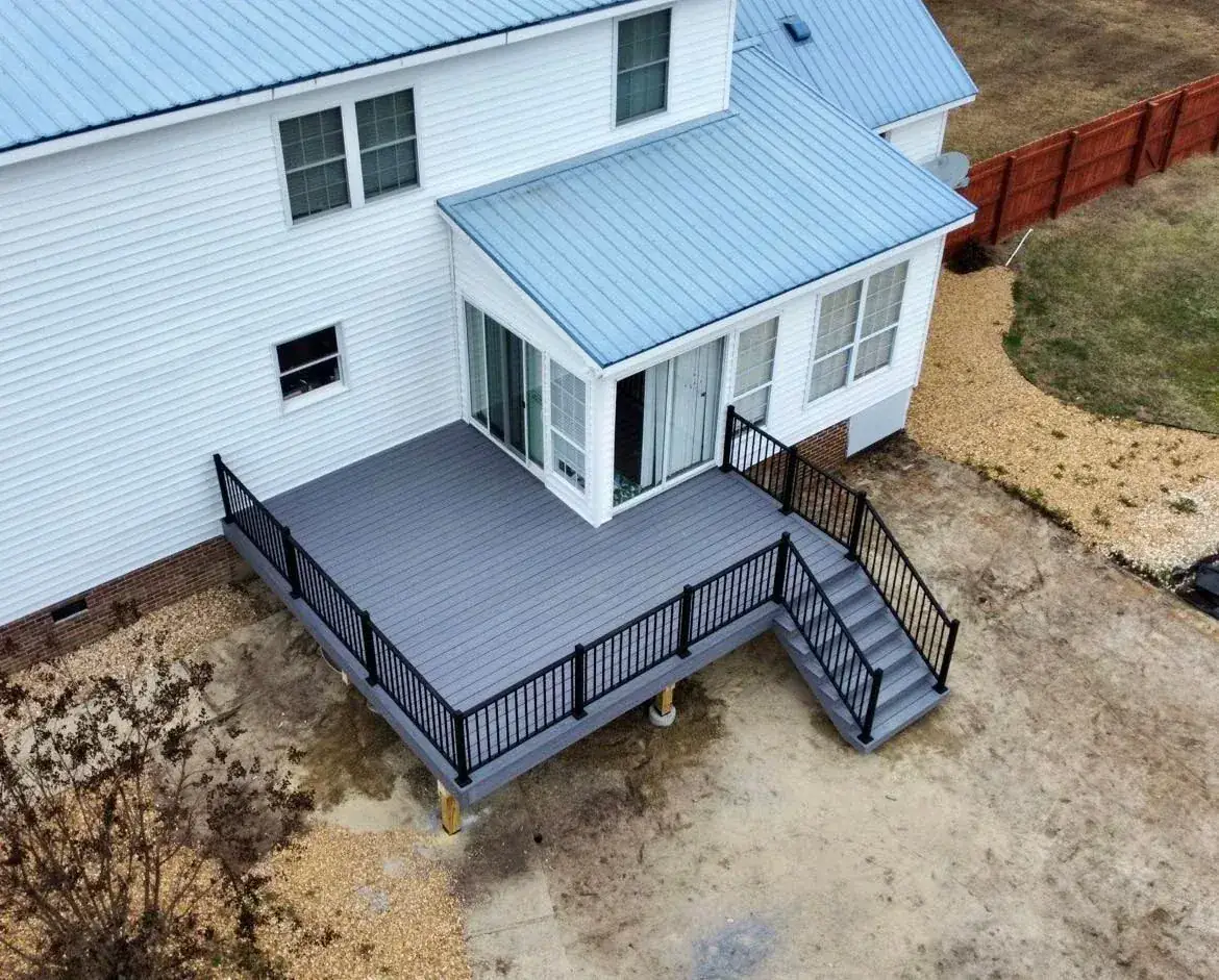 Gray composite deck with black railing connected to a windowed sunroom