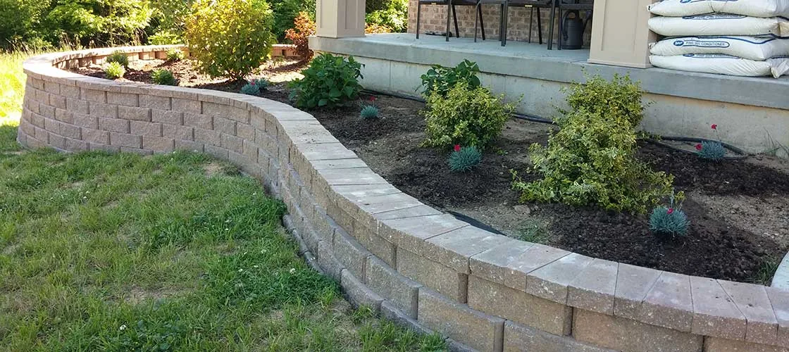 Low curved block retaining wall framing a mulched garden bed with shrubs and flowers