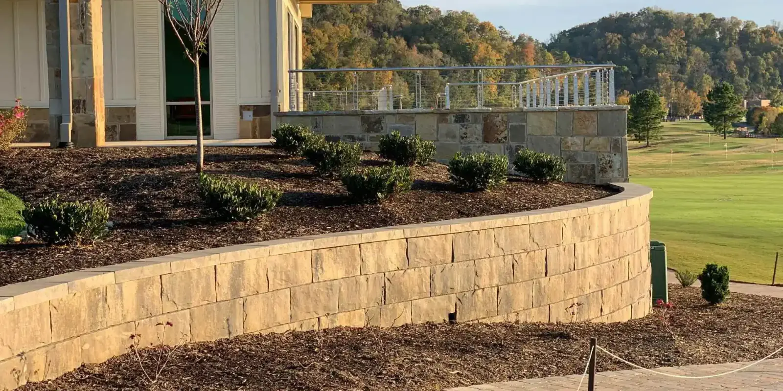 Block retaining wall supporting a mulched shrub bed beside a home