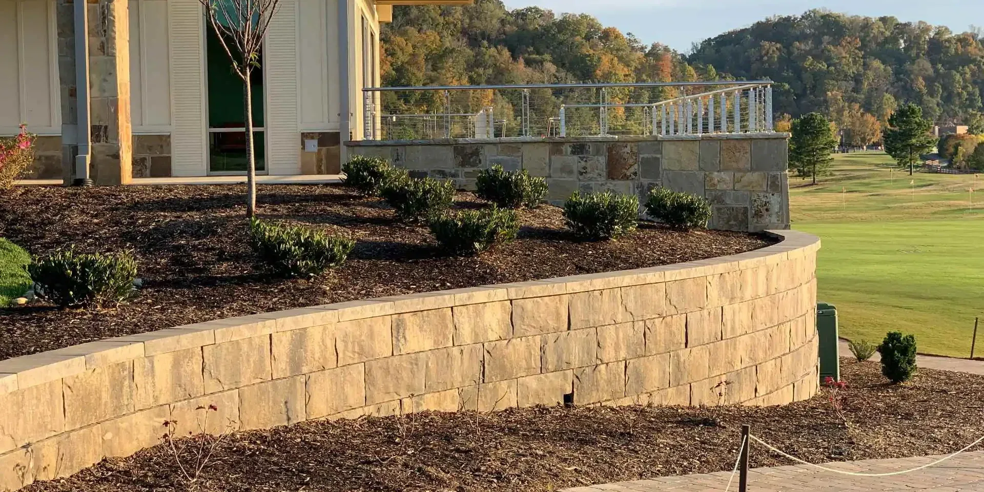 Curved tan stone retaining wall defining a landscaped terrace beside a building