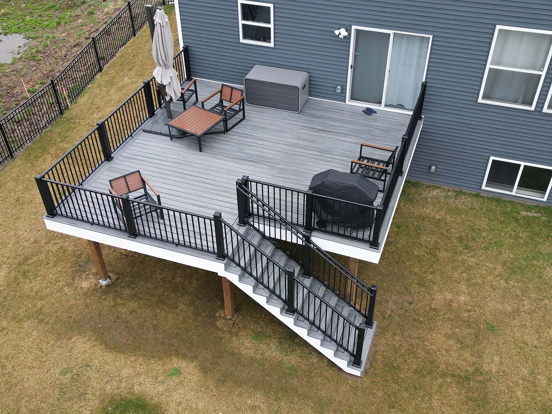 Elevated gray composite deck with black railing, stairs, seating, and a grill