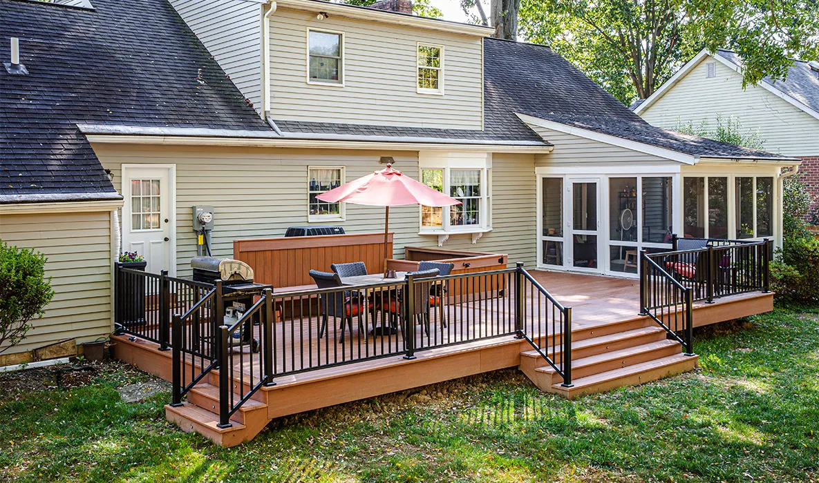 Backyard deck with black metal railing, steps, outdoor dining furniture, and a grill.