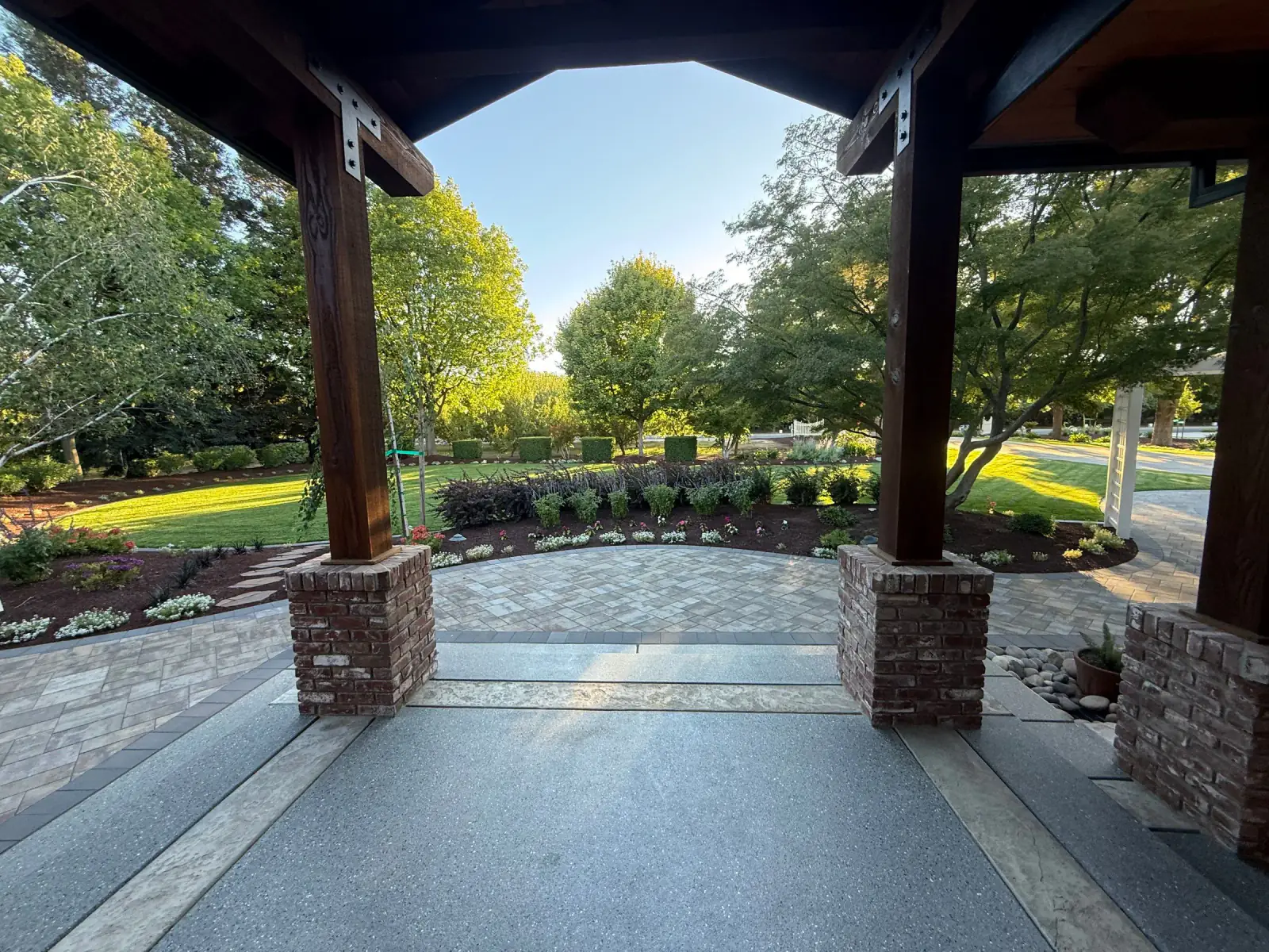 View from a covered patio across planting beds, lawn, and mature trees