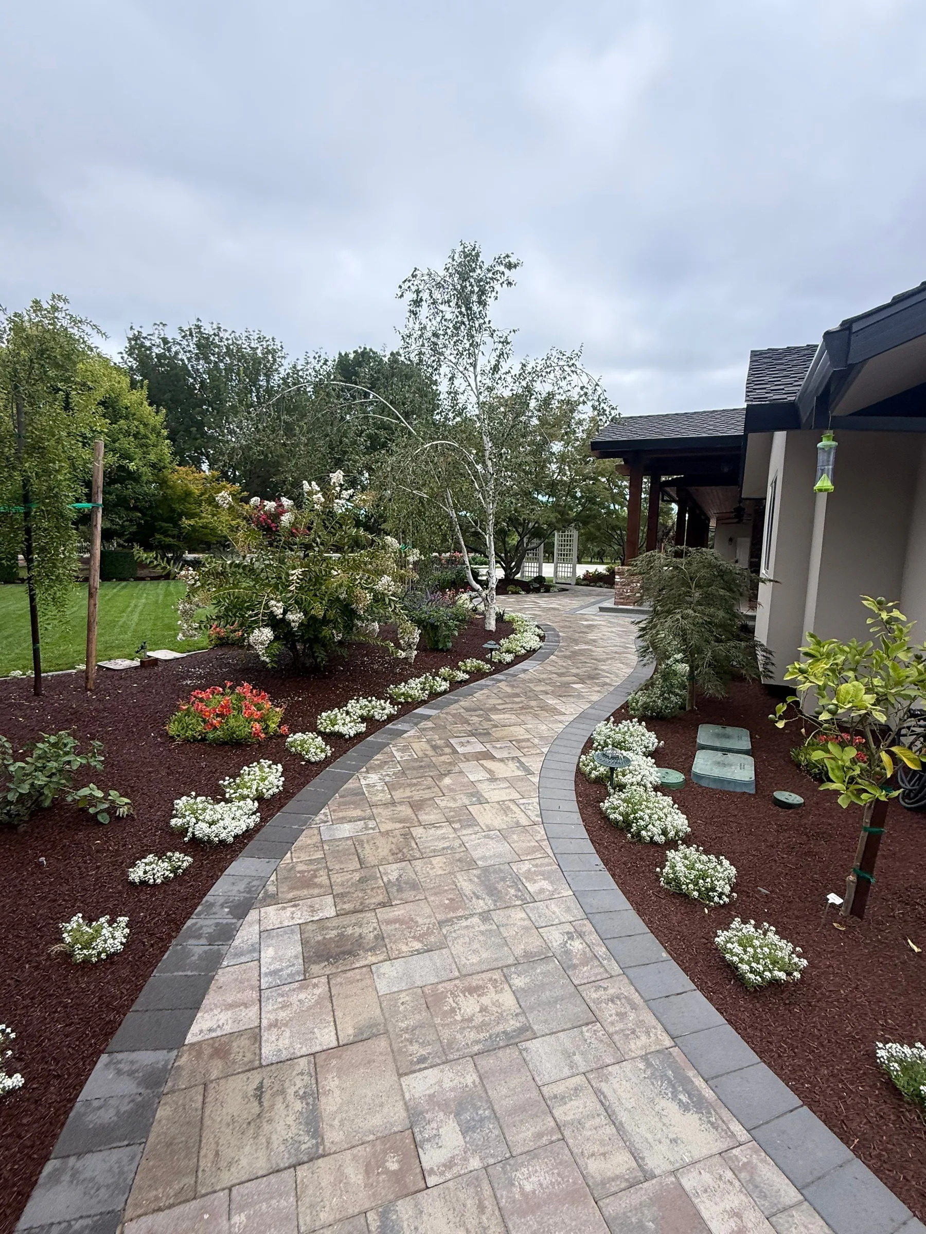 Curved paver path passing through established planting beds beside a home