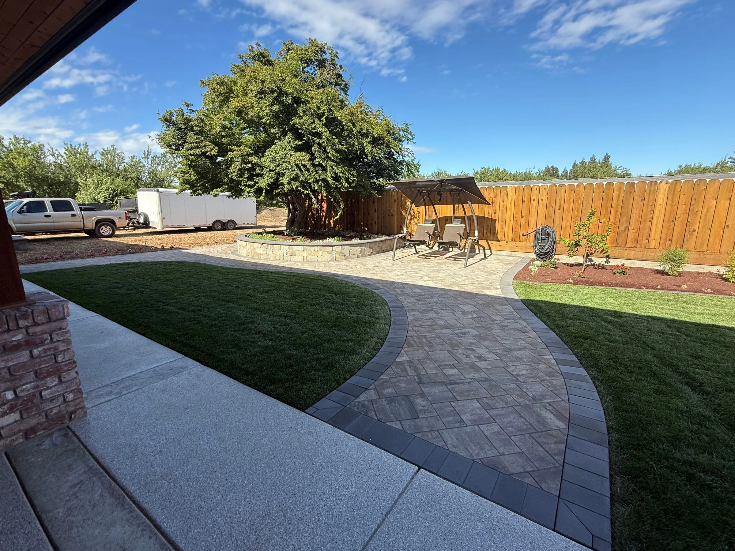 Curved paver path crossing a lawn toward a pergola and fenced backyard