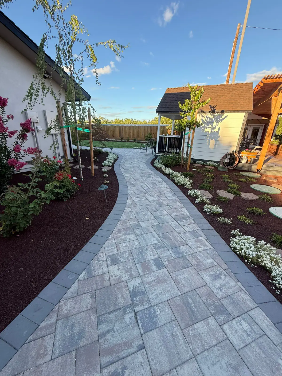 Curved paver walkway connecting planting areas with a backyard structure