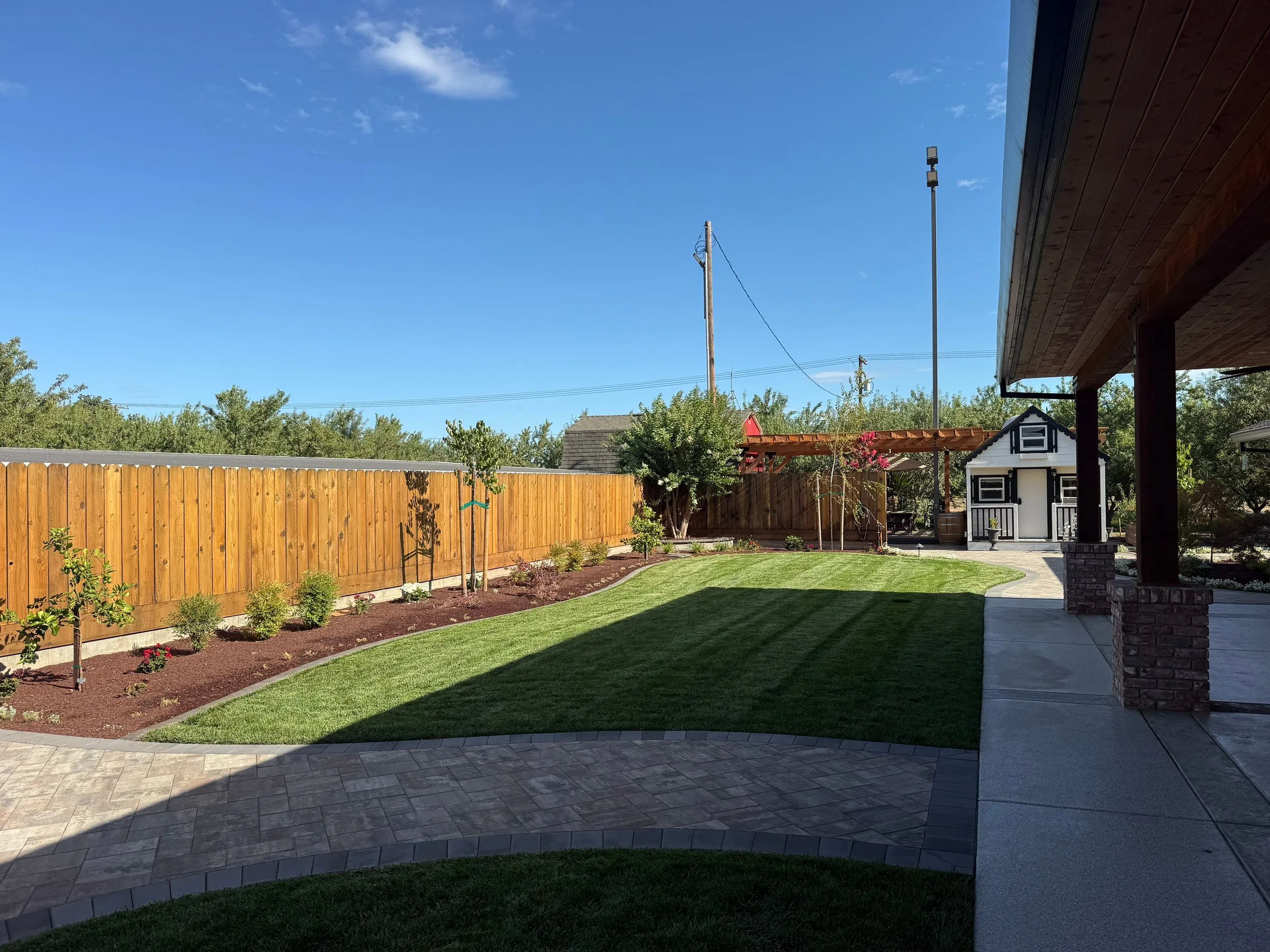 Landscaped backyard with a green lawn, young trees, planting beds, and a wood fence