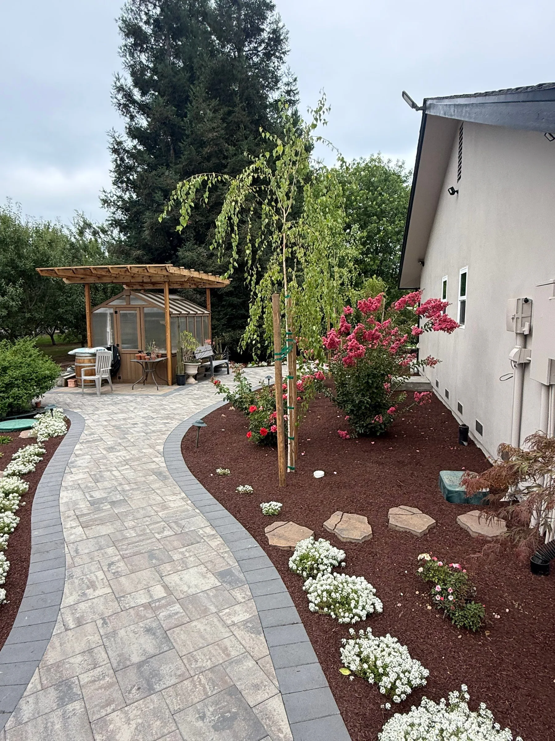 Paver walkway leading toward a pergola and landscape