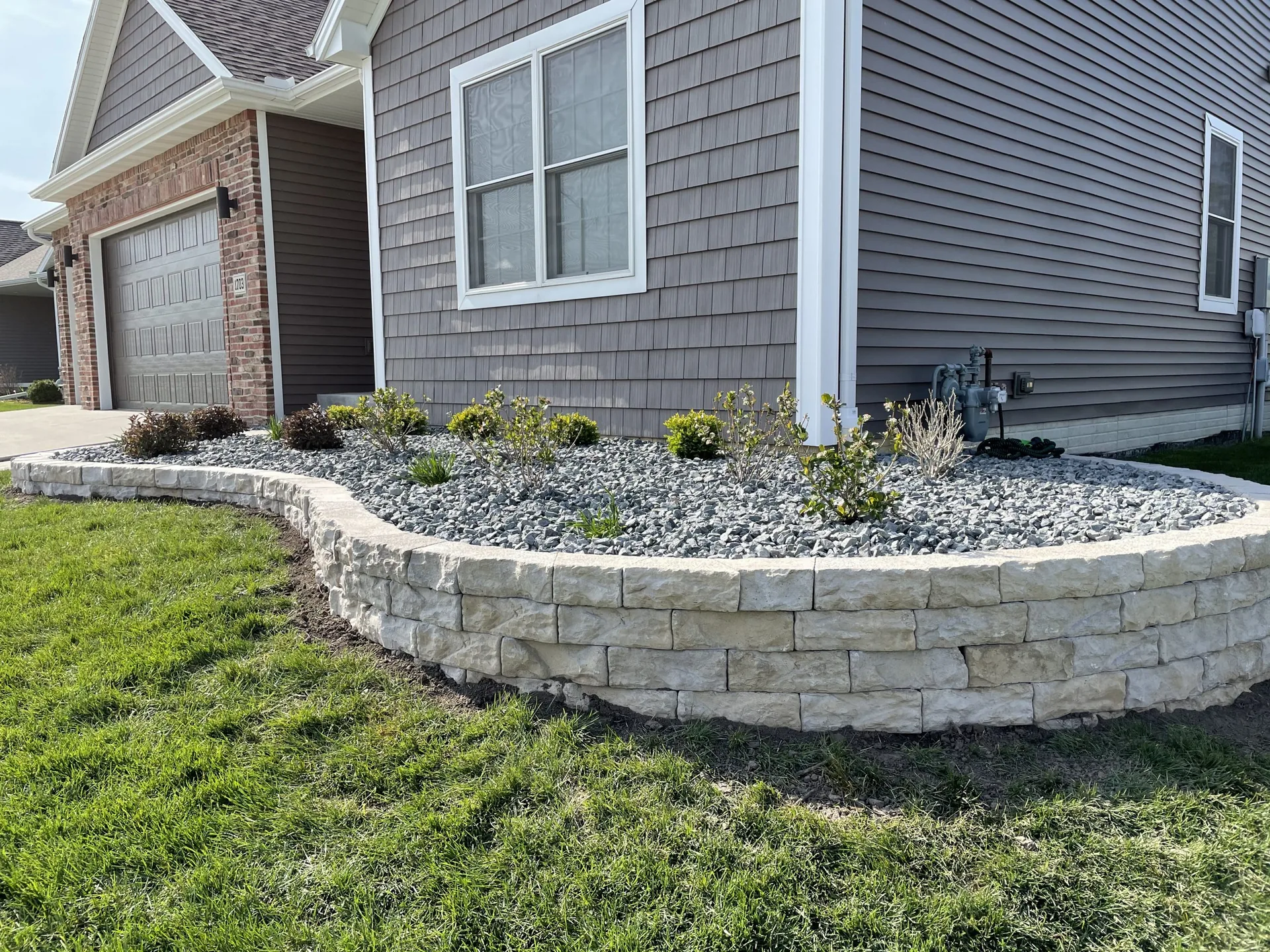 Curved stone retaining wall defining a raised landscape bed beside a home